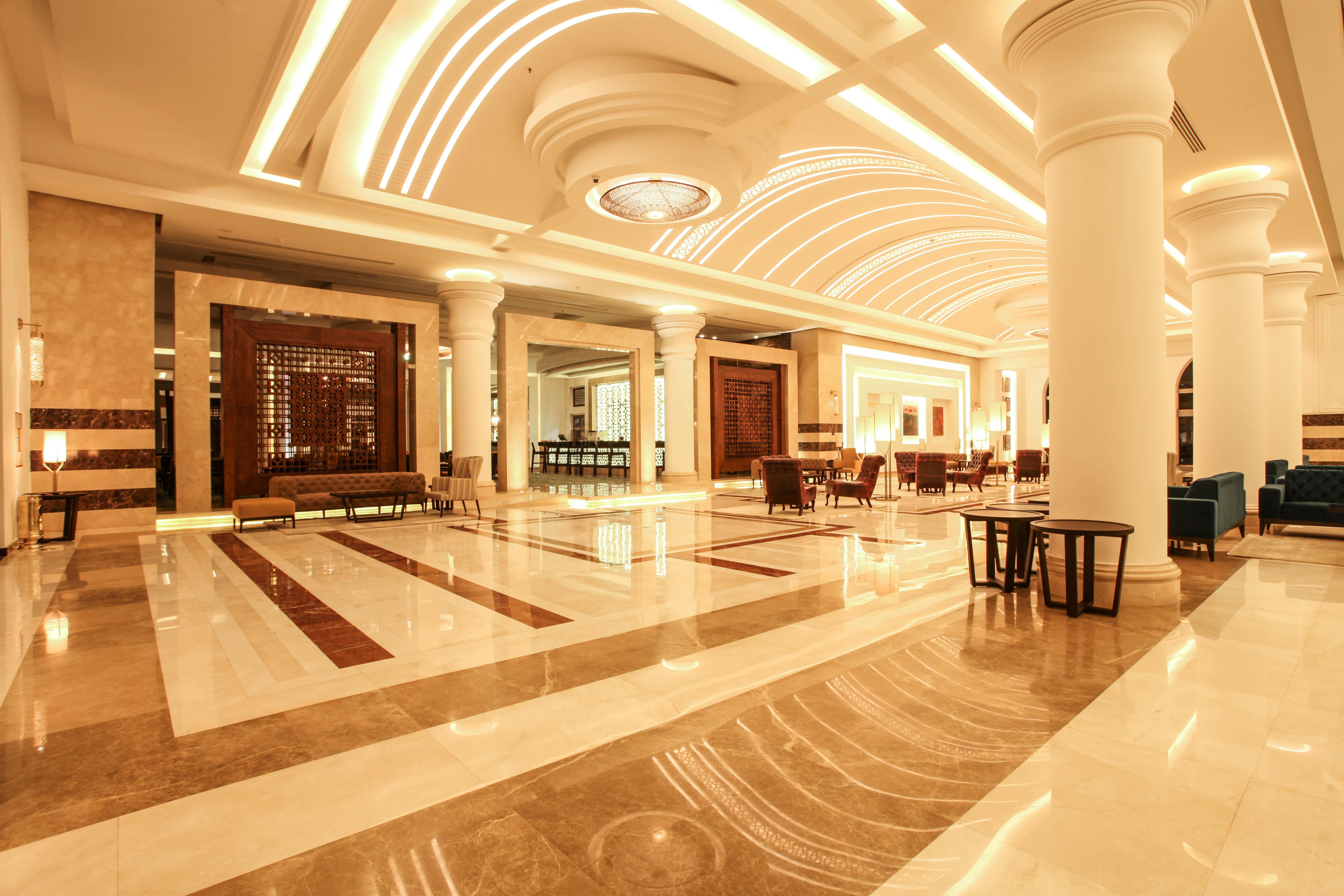 Savoy Le Grand Hotel Marrakech Marrakesz Zewnętrze zdjęcie The photo shows an elegant hotel lobby with a spacious and luxurious design. The floor features a mix of light and dark marble patterns, creating an appealing visual contrast. The ceiling has a modern, curved design with soft lighting that enhances t