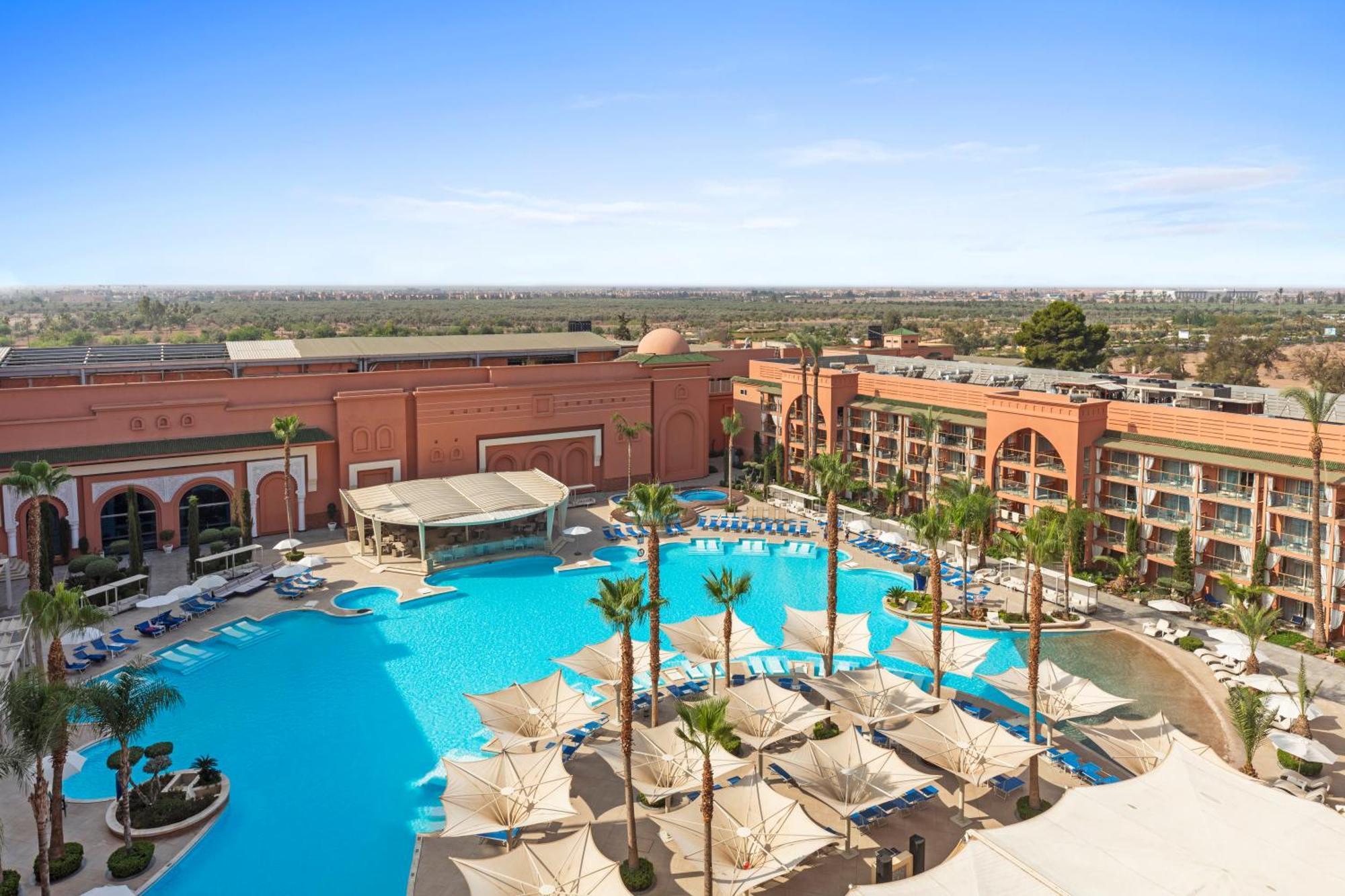 Savoy Le Grand Hotel Marrakech Marrakesz Zewnętrze zdjęcie The photo depicts a stylish resort pool area surrounded by palm trees. It features a large, inviting swimming pool with a spacious deck and lounge chairs arranged around it. There are shaded cabanas or umbrellas providing sun protection for guests. I