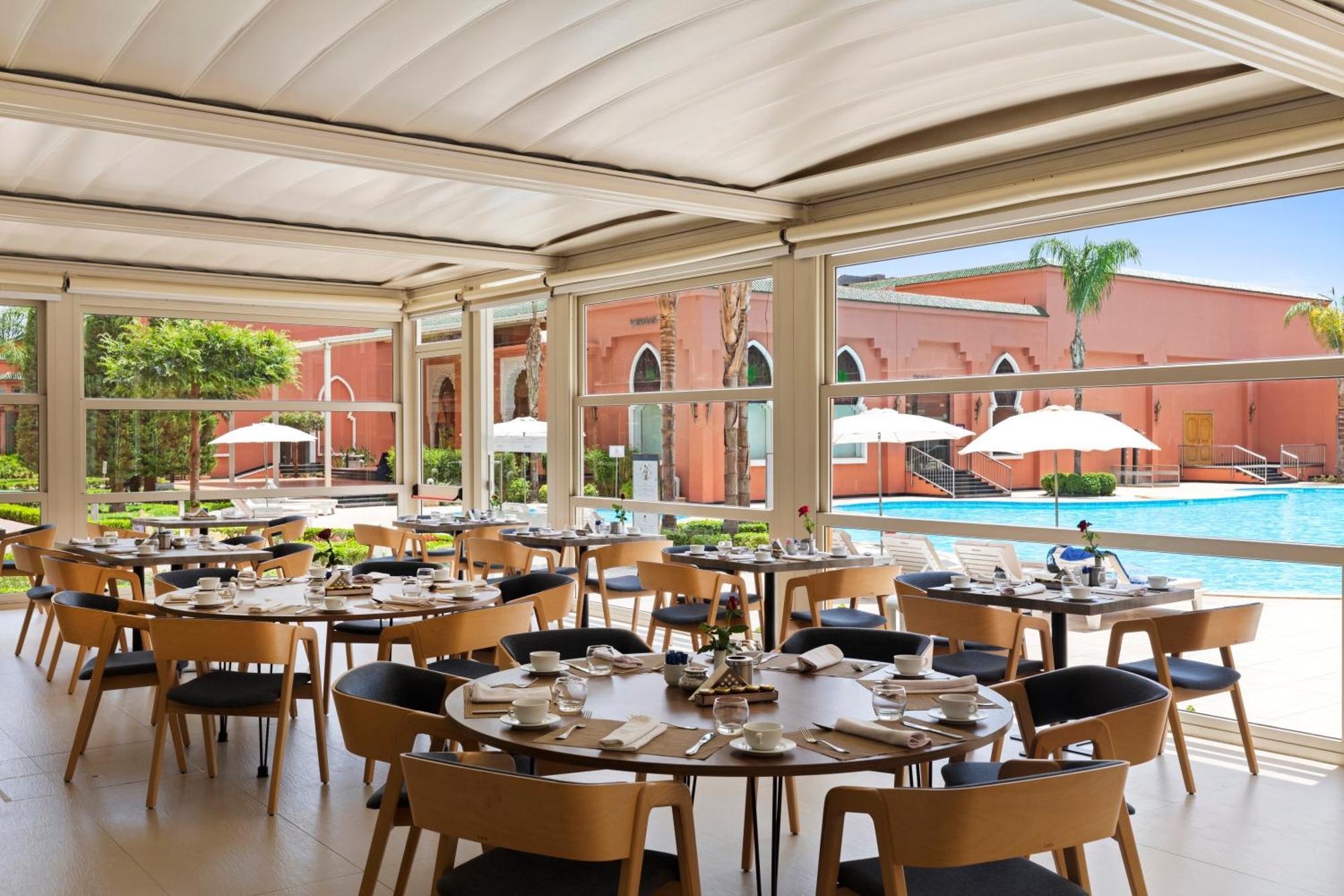 Savoy Le Grand Hotel Marrakech Marrakesz Zewnętrze zdjęcie The photo shows a modern restaurant setting with several round tables arranged for dining. Each table is neatly set with plates, glasses, and cutlery. The restaurant features large windows that allow plenty of natural light to flood in, offering a vi